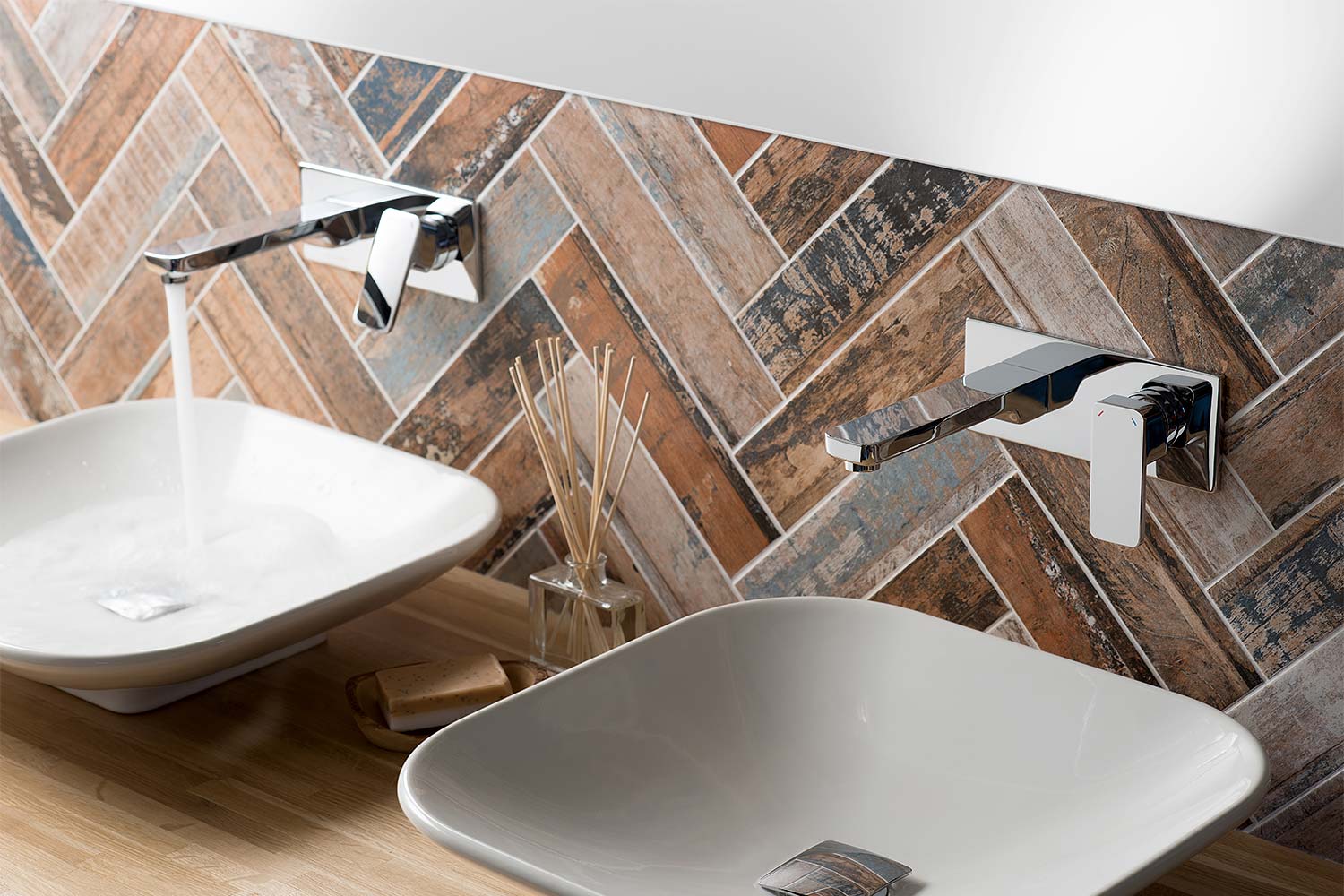 a pair of wall mounted single lever basin mixers on a parquet tiled wall over a pair of white square bowls.