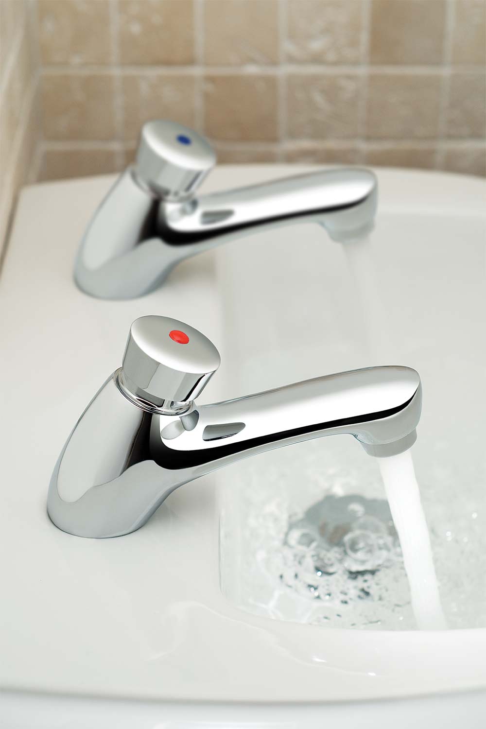 A pair of non-concussive push-type basin pillar taps with flowing water on a white basin.