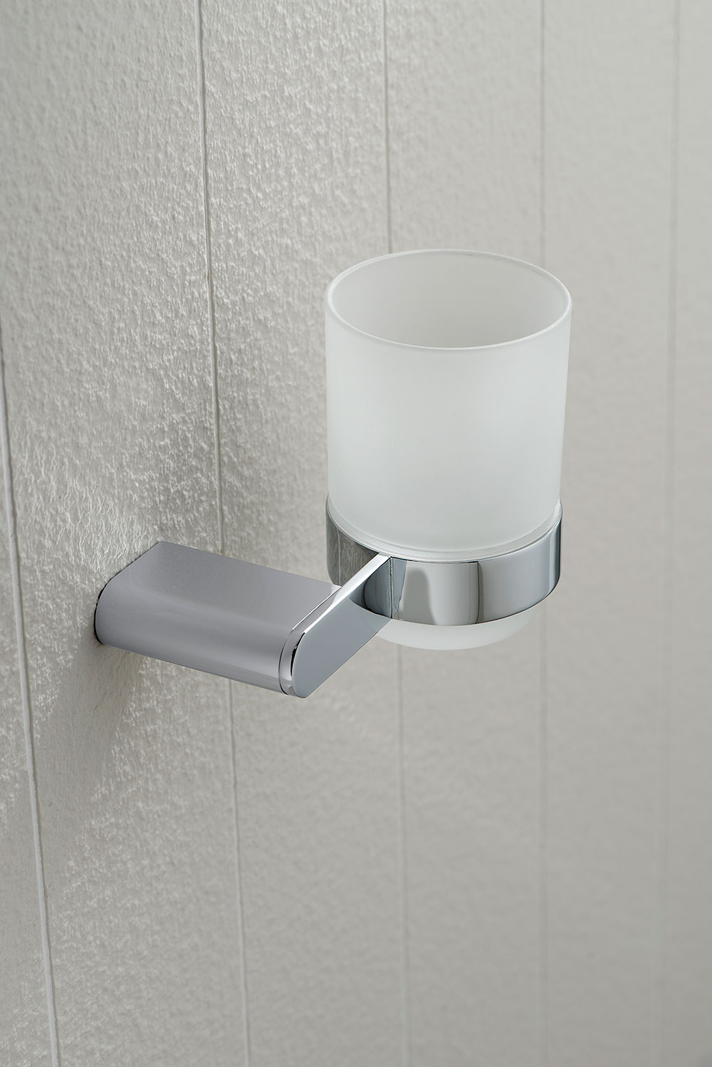 Modern frosted glass tumbler and chrome holder on a white linear pattern wall.