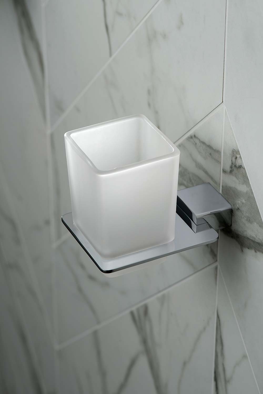 Modern chrome square tumbler and holder on diagonal marble tiles.