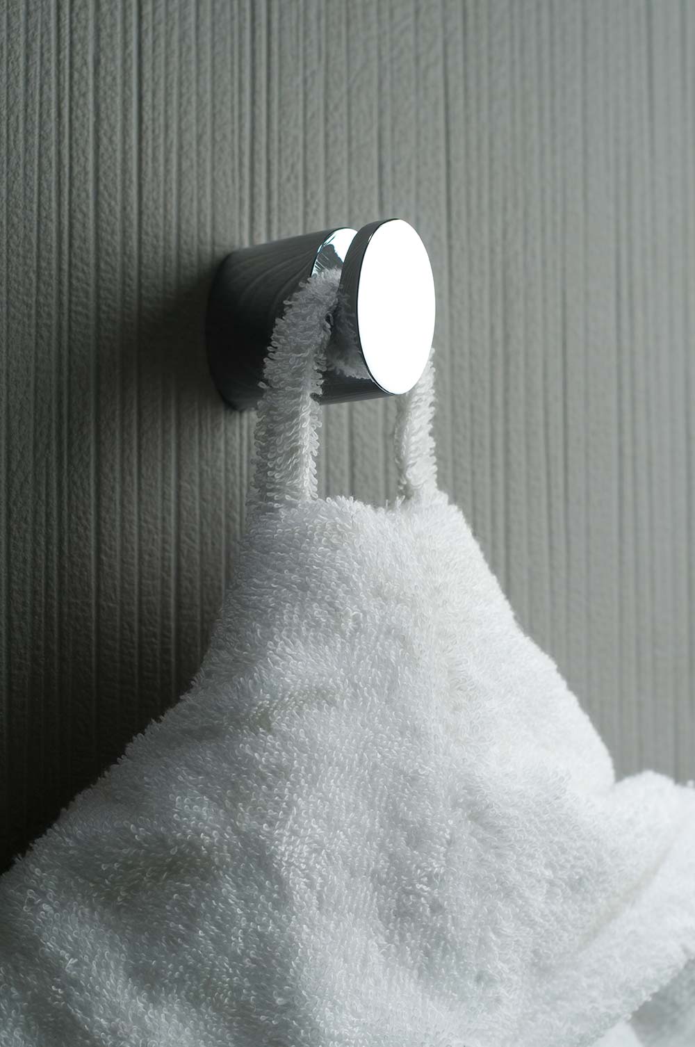 A chrome oval robe hook on a grey wall with a white dressing gown.