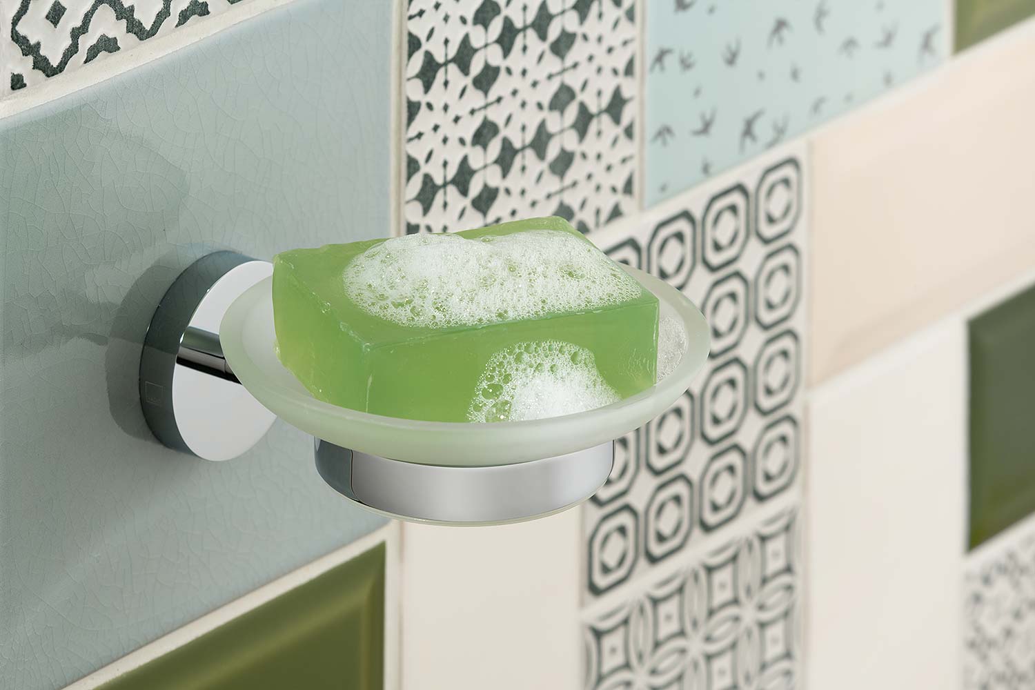 Round frosted glass with a green bar of soap and chrome holder on a funky tiled wall.