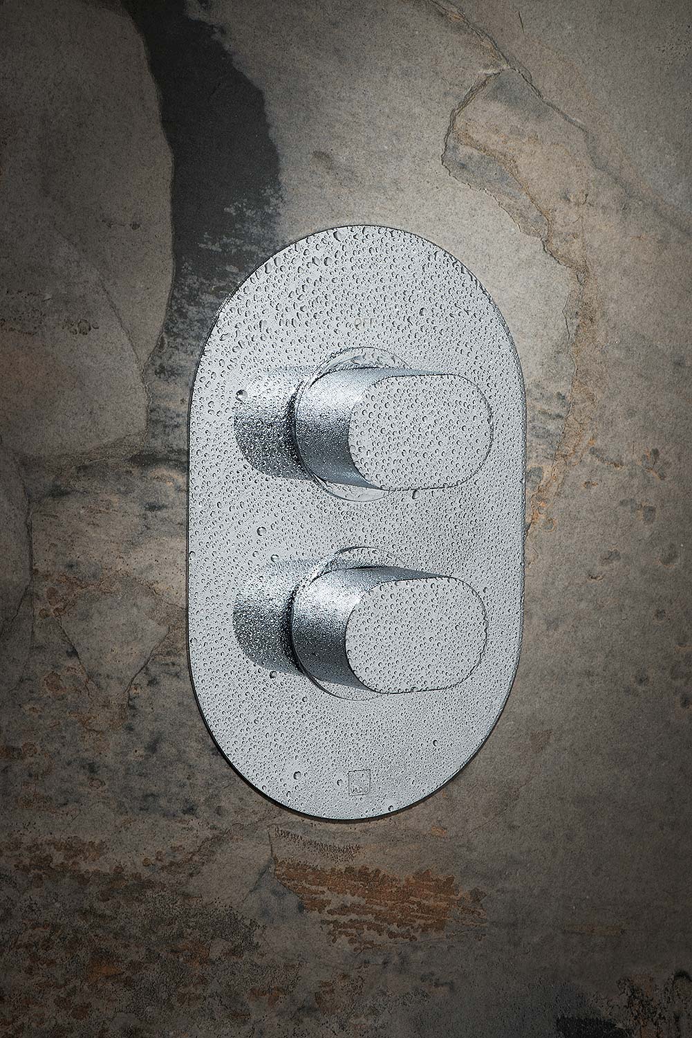 Two handle thermostatic shower valve covered in water drops on a brown tile