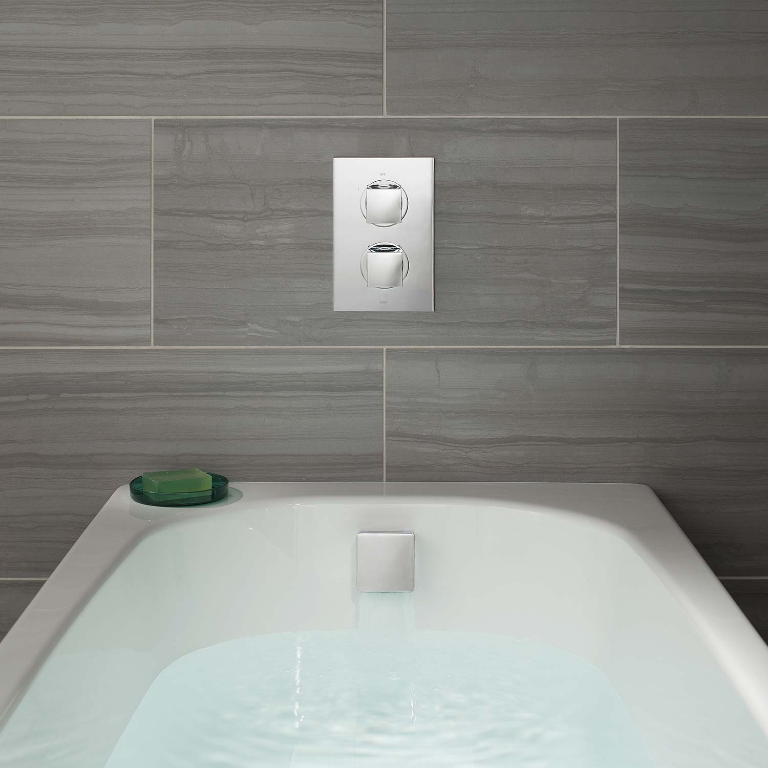 A bath full of water with a rectangular thermostatic valve and square bath filler waste overflow.