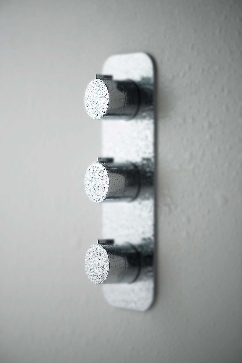 Side view of a three handle shower valve with water drops