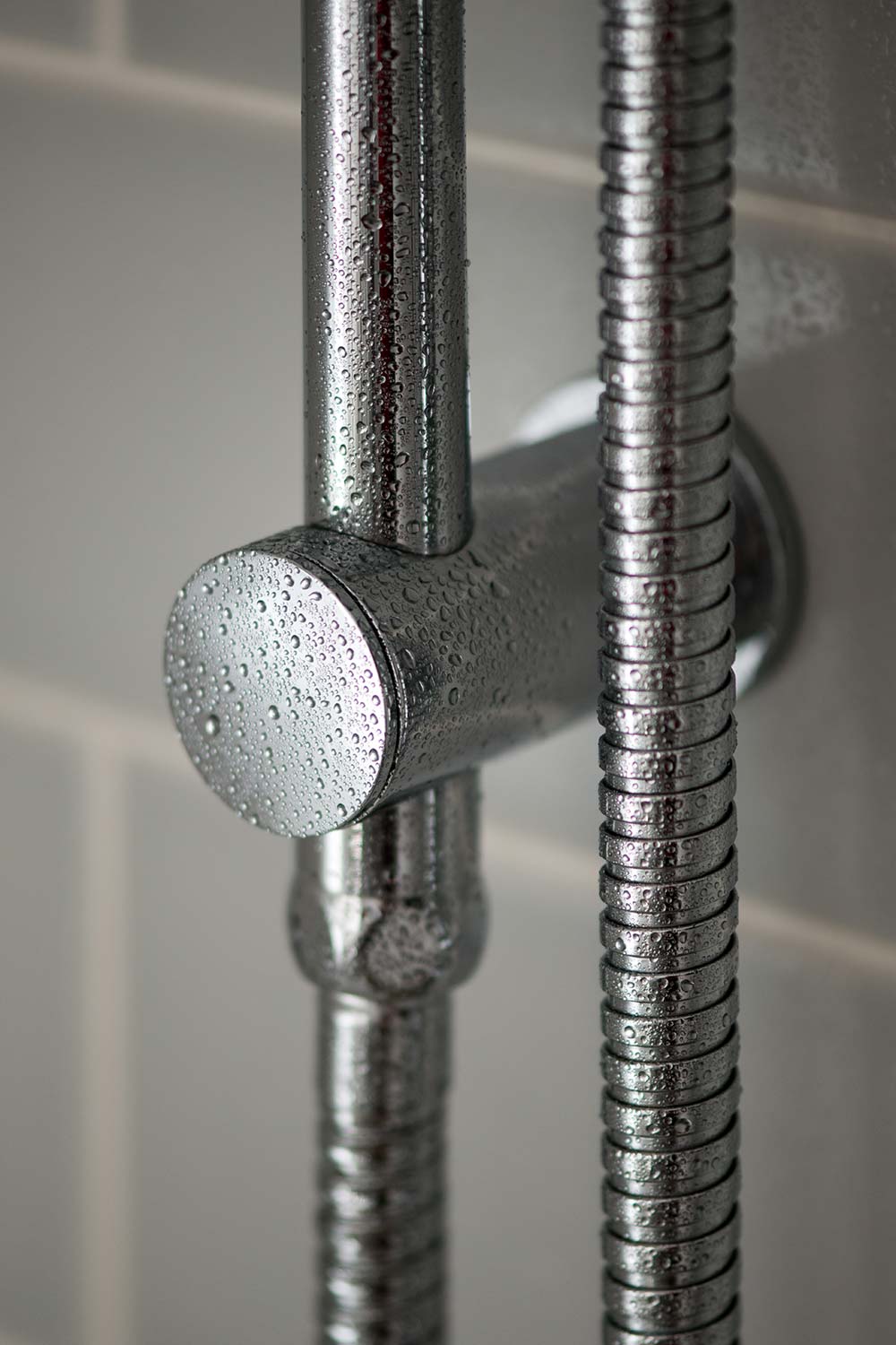 Close up of a shower rail and hose covered in water drops.