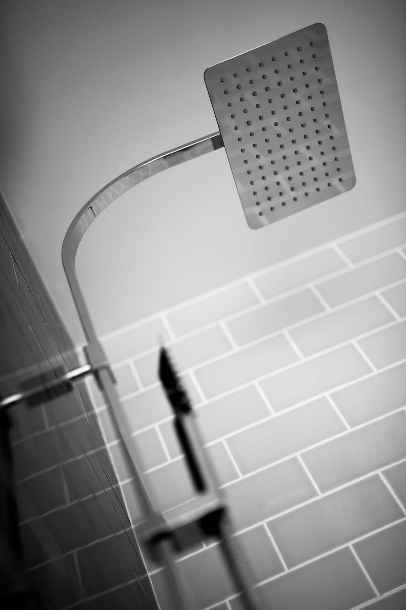 Shallow depth-of-field photograph of a shower riser, head and handset, focussing on the handset