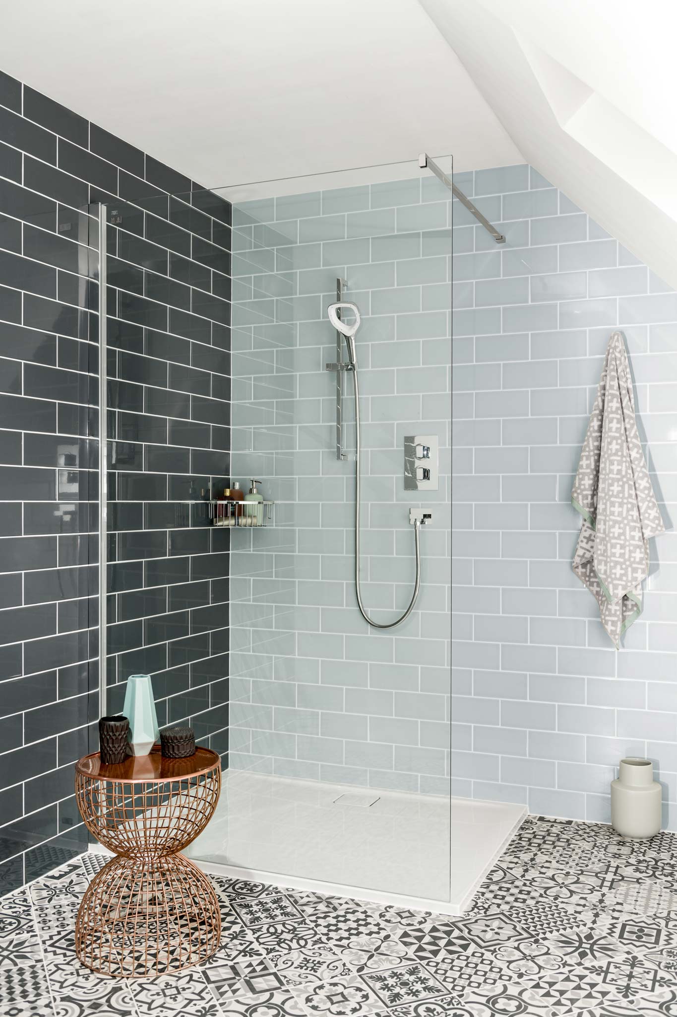 A shower tray and screen with tiles walls and floor in an attic under a sloping roof