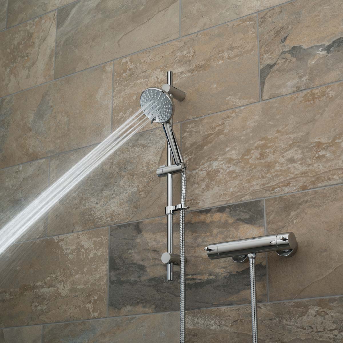 A slide rail shower kit with an exposed thermostatic bar type valve on a brown tiled wall with a narrow spray pattern
