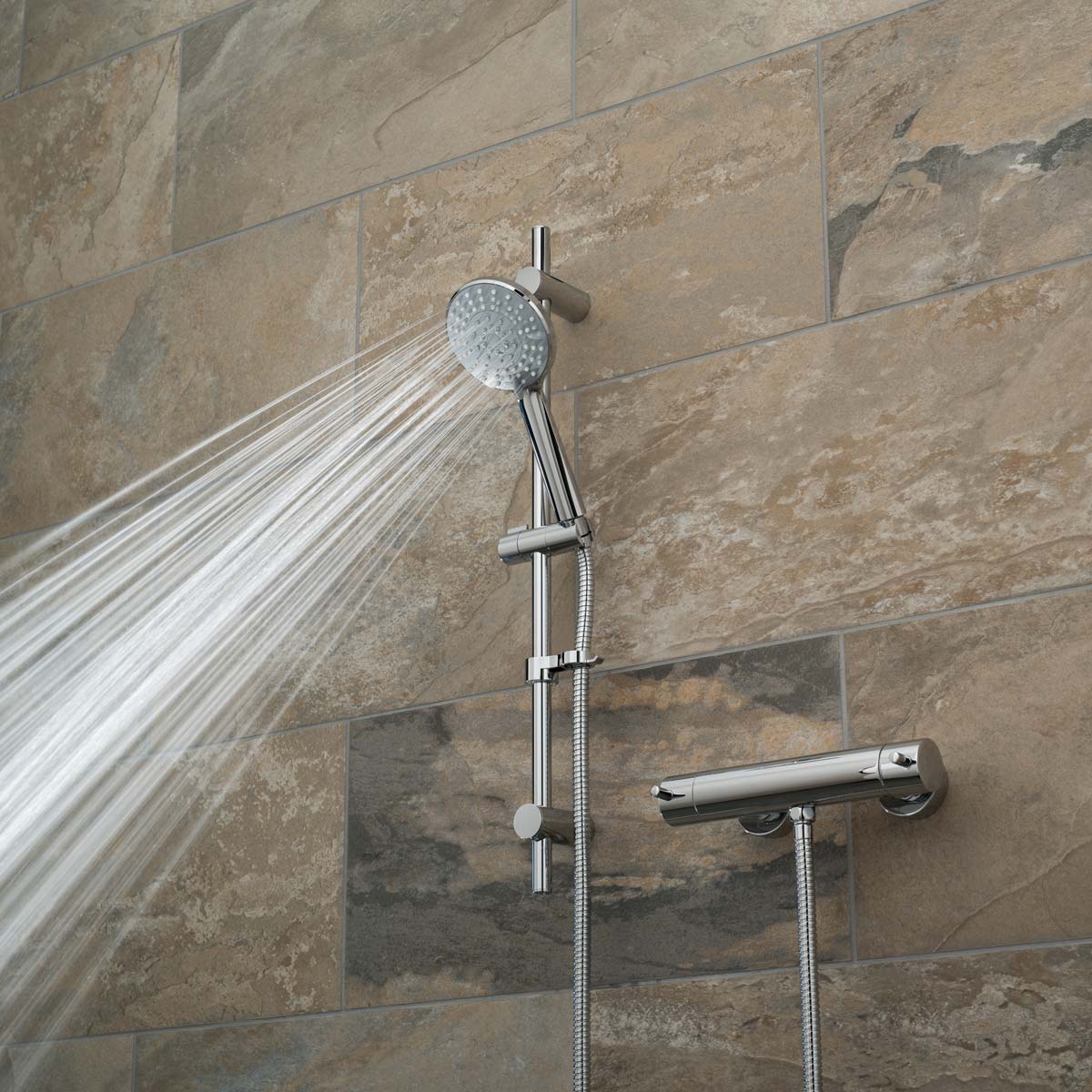 A slide rail shower kit with an exposed thermostatic bar type valve on a brown tiled wall with a wide spray pattern