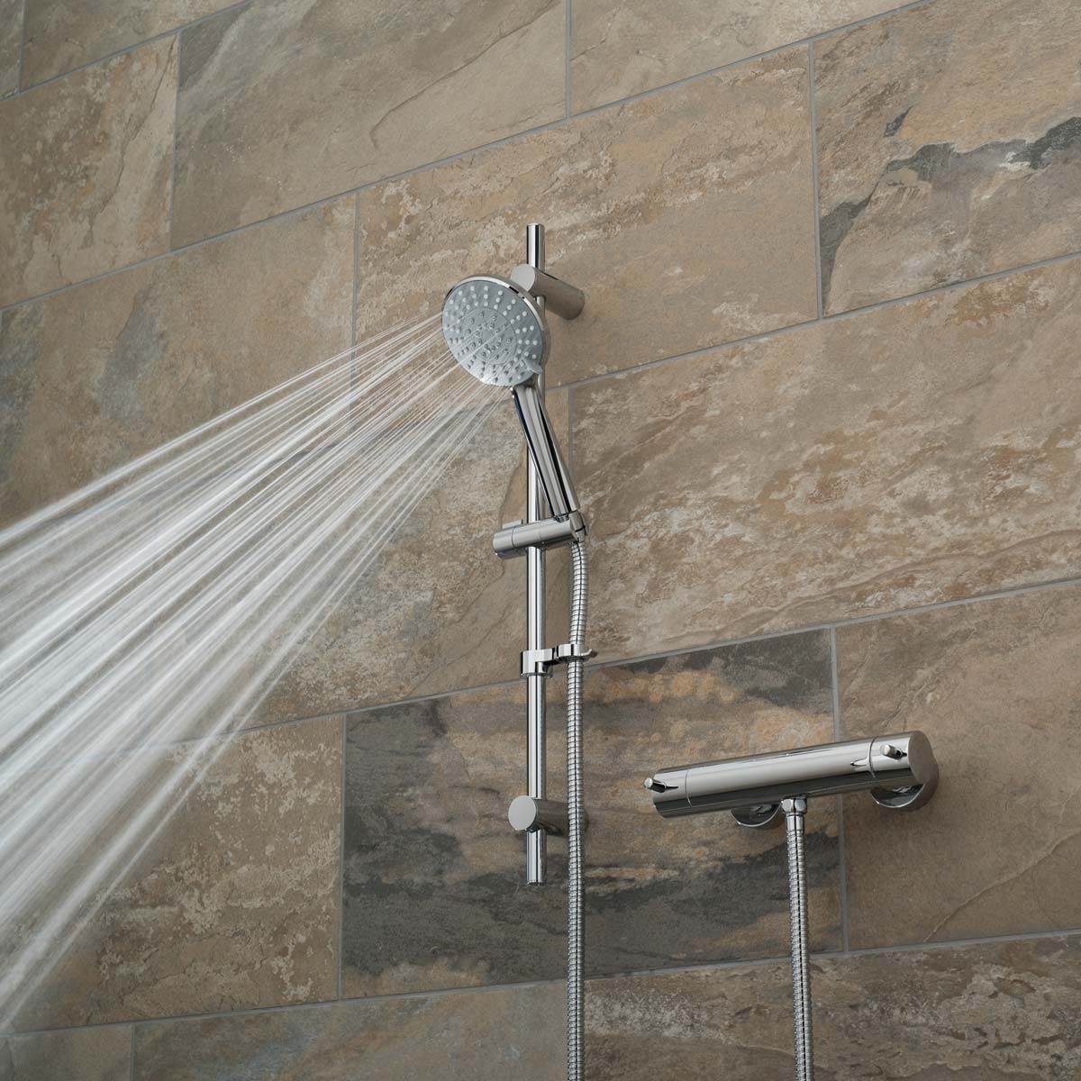 A slide rail shower kit with an exposed thermostatic bar type valve on a brown tiled wall with a wide spray pattern