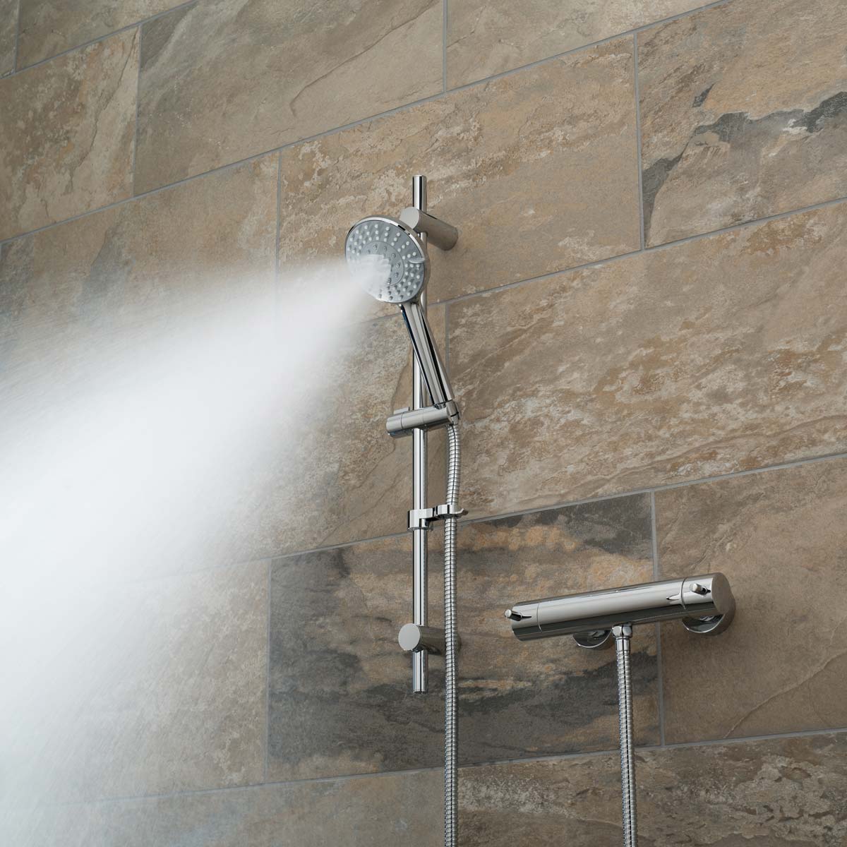 A slide rail shower kit with an exposed thermostatic bar type valve on a brown tiled wall with a mist spray pattern