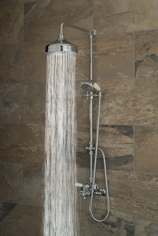 Traditional exposed shower mixer with a rigid riser, deluge shower head and handset on a brown tiled wall, with water cascading out of the shower head.