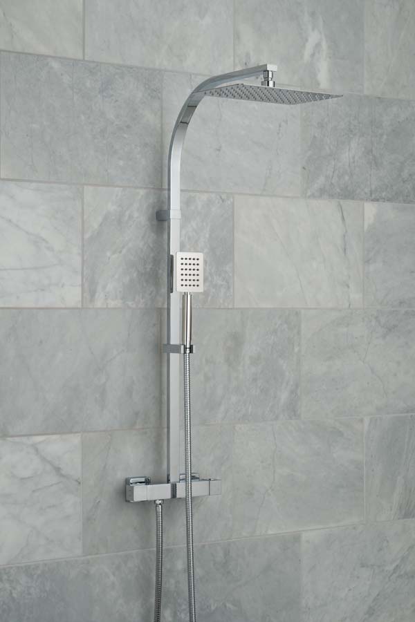 Modern exposed shower mixer with a rigid riser, deluge shower head and handset on a marble tiled wall, with water cascading out of the shower head.