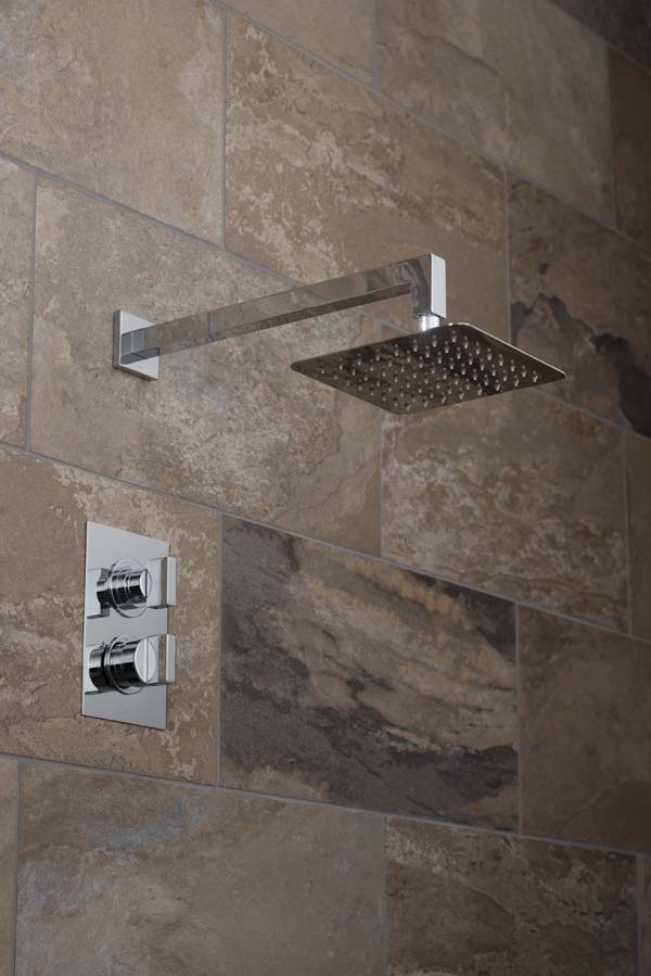 Square shower head and arm with a rectangular concealed thermostatic shower valve on a brown slate tiled wall.