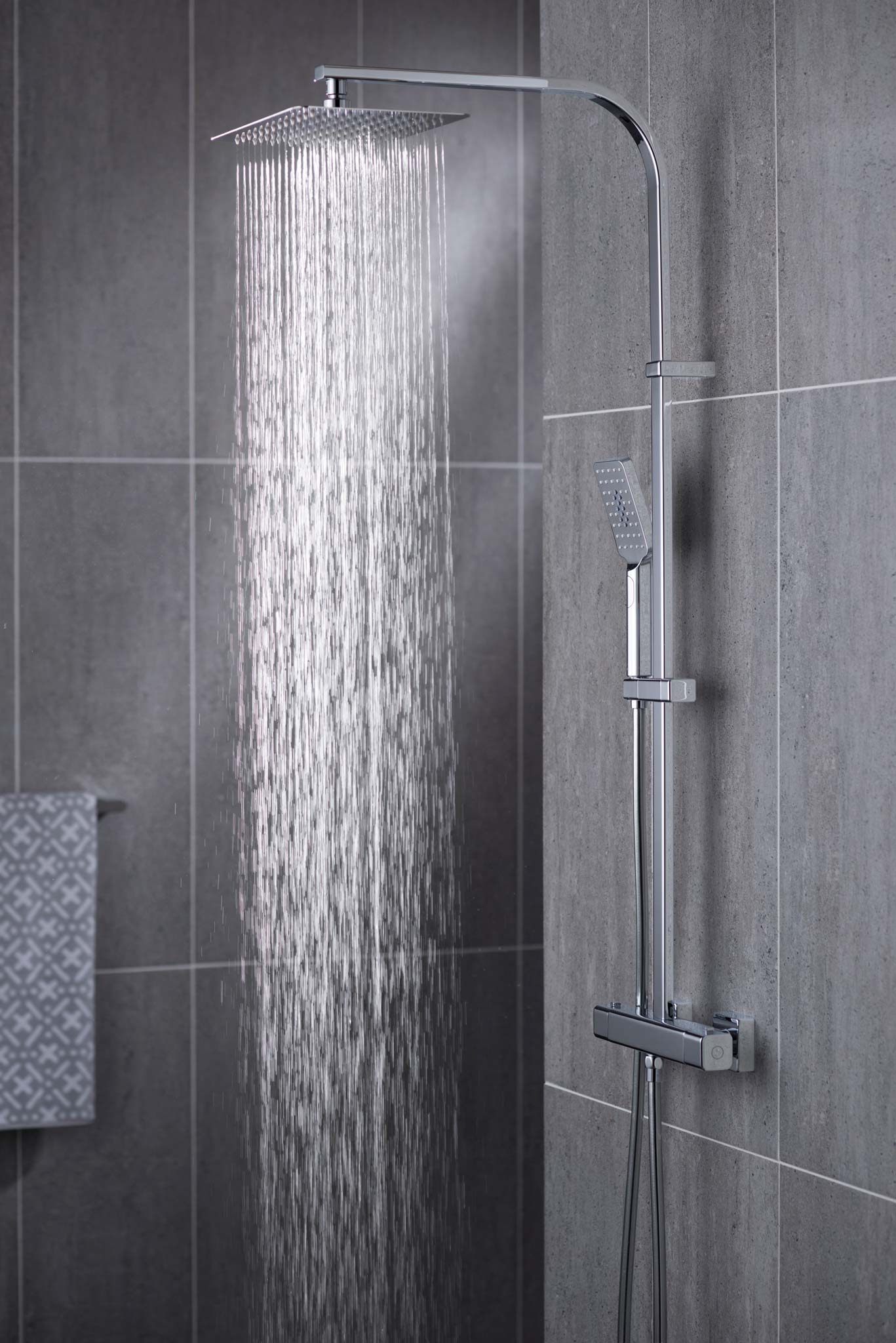 Modern rectangular rigid riser in a grey tiled room with water cascading out of the shower head a towel in the background