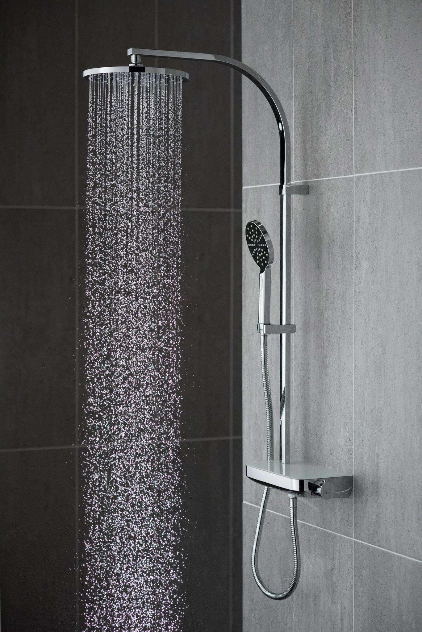 Modern round rigid riser in a grey tiled room with water cascading out of the shower head, shutter speed 1/2500th second to freeze the water.