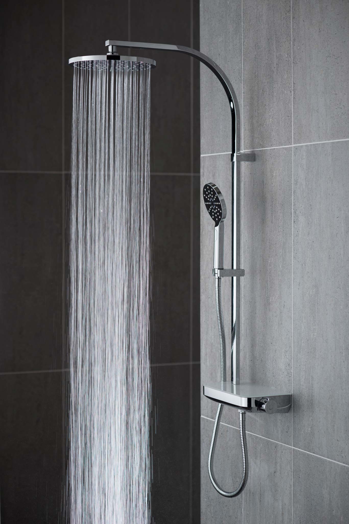 Modern round rigid riser in a grey tiled room with water cascading out of the shower head, shutter speed 1/40th second