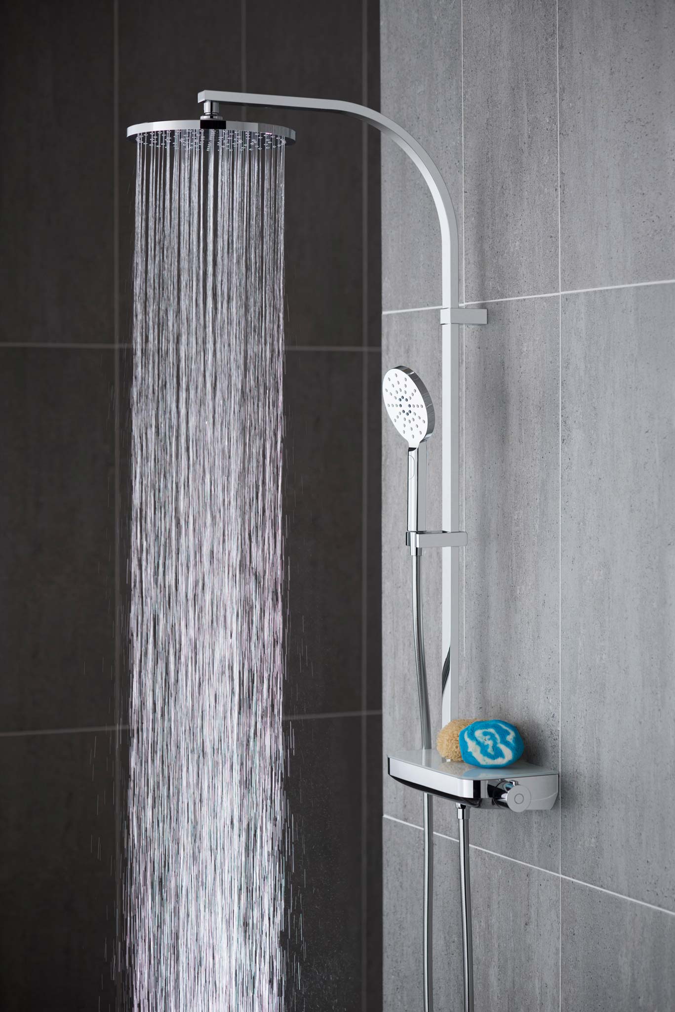 Modern round rigid riser in a grey tiled room with water cascading out of the shower head.