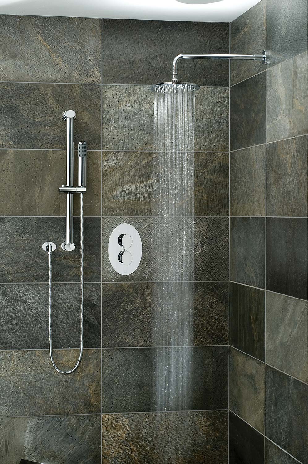 Tiled bathroom with a slide rail shower kit, shower arm and head, and oval thermostatic valve with and water cascading from the shower head