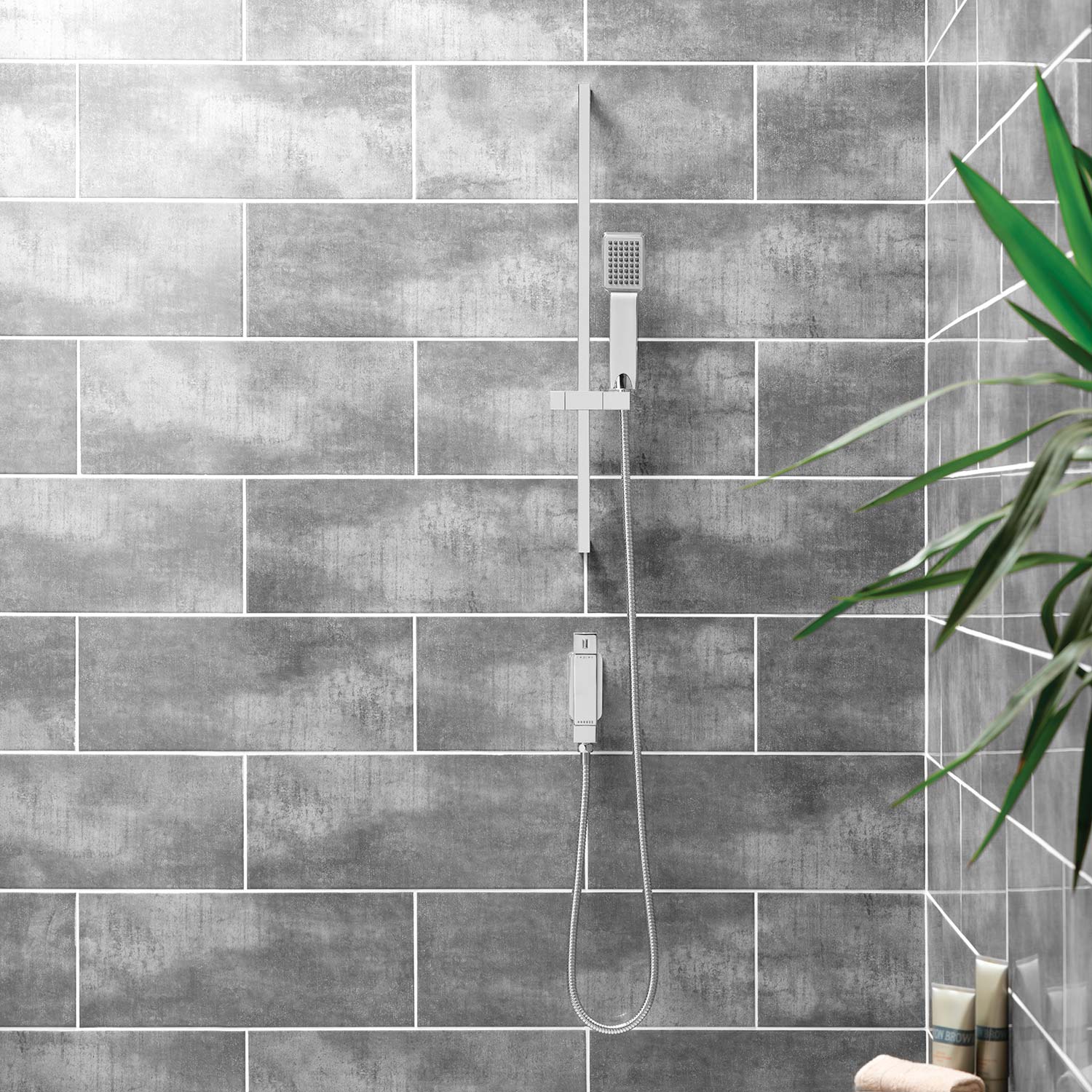 A Slide rail shower kit on a large brown tiled wall with a green plant in the foreground.